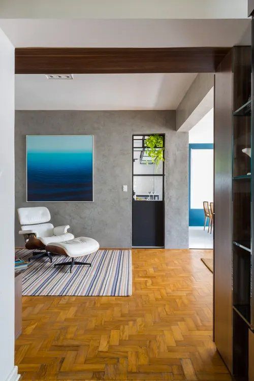 Uma sala com cadeira e pufe e uma pintura na parede.