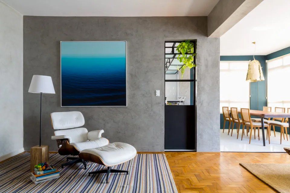 Uma sala com cadeira e pufe e uma pintura na parede.