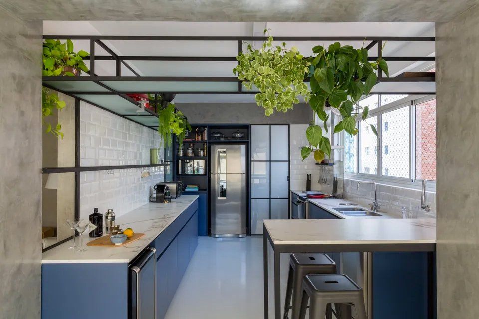 Uma cozinha com armários azuis, geladeira, pia, mesa e plantas penduradas no teto.