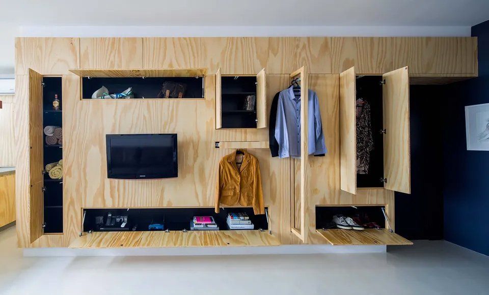 Uma parede de madeira com uma televisão e roupas penduradas.