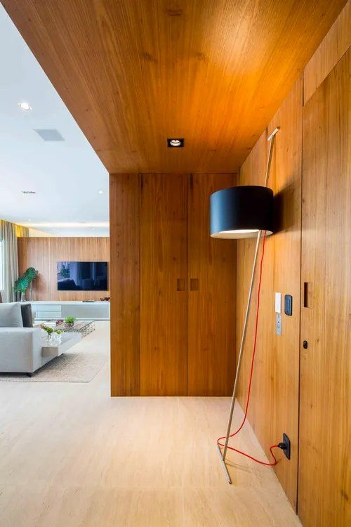 Uma lâmpada está pendurada em uma parede de madeira em um corredor que leva a uma sala de estar.