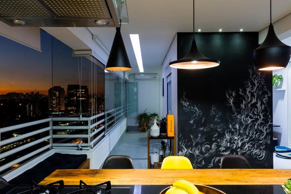 Uma cozinha com mesa e cadeiras e uma varanda com vista para a cidade à noite.