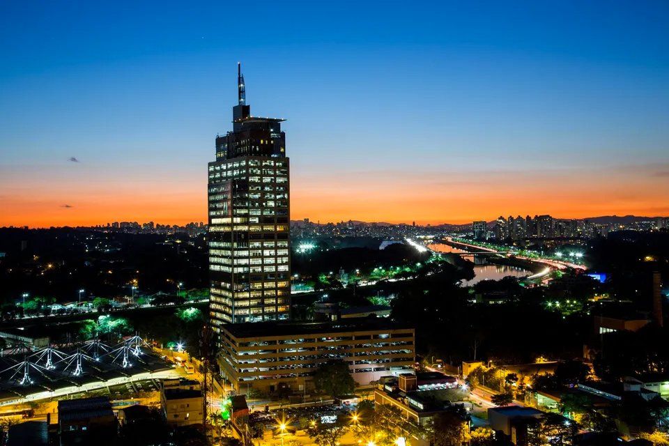 Uma vista aérea de uma cidade à noite com um prédio alto em primeiro plano.