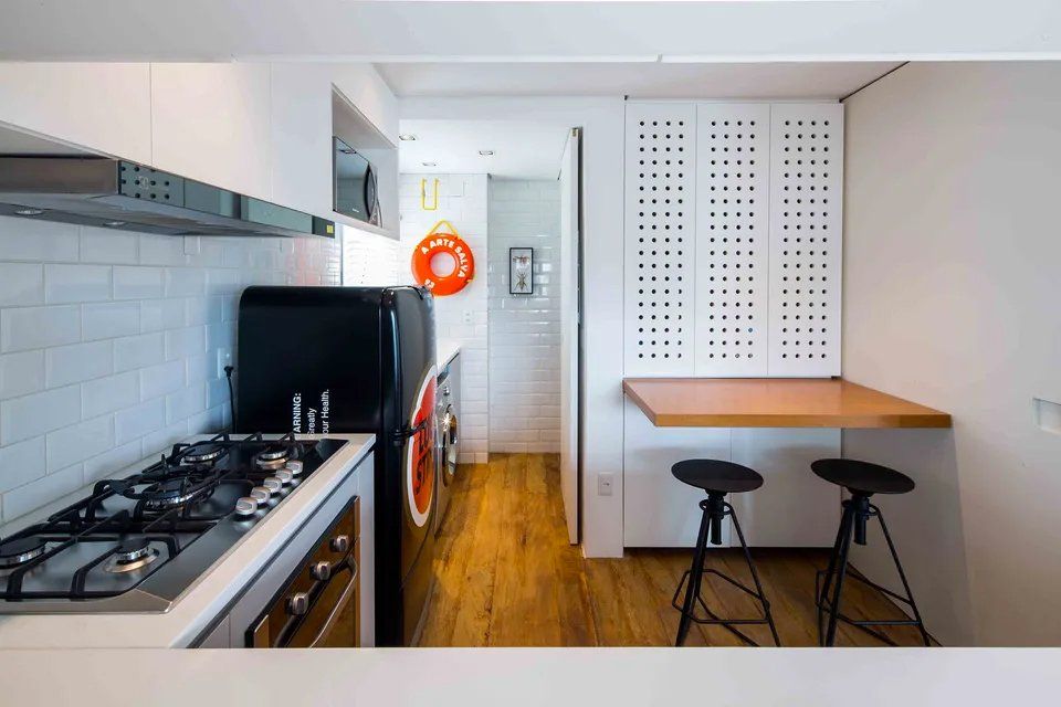 Uma cozinha com fogão, forno, geladeira e bancos.