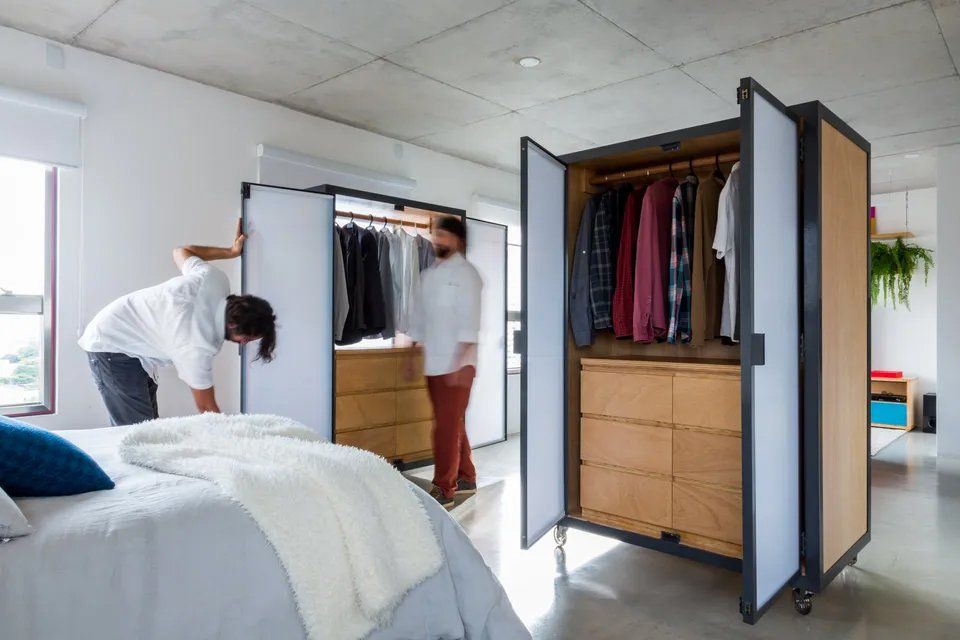 Dois homens estão em um quarto olhando dentro de um guarda-roupa.