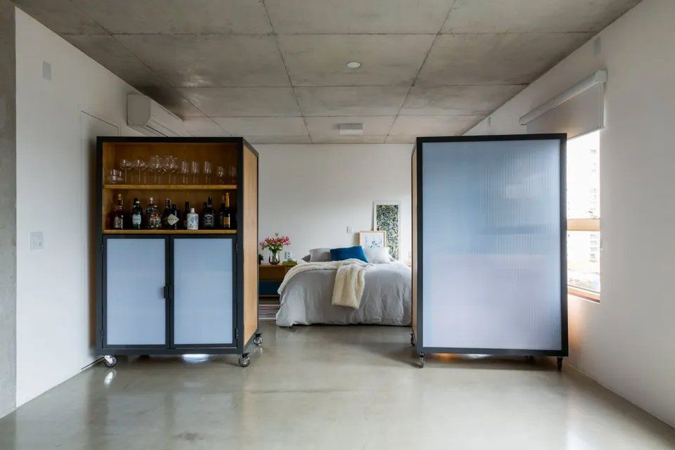 Um quarto com cama, bar e divisória entre o quarto e a sala.