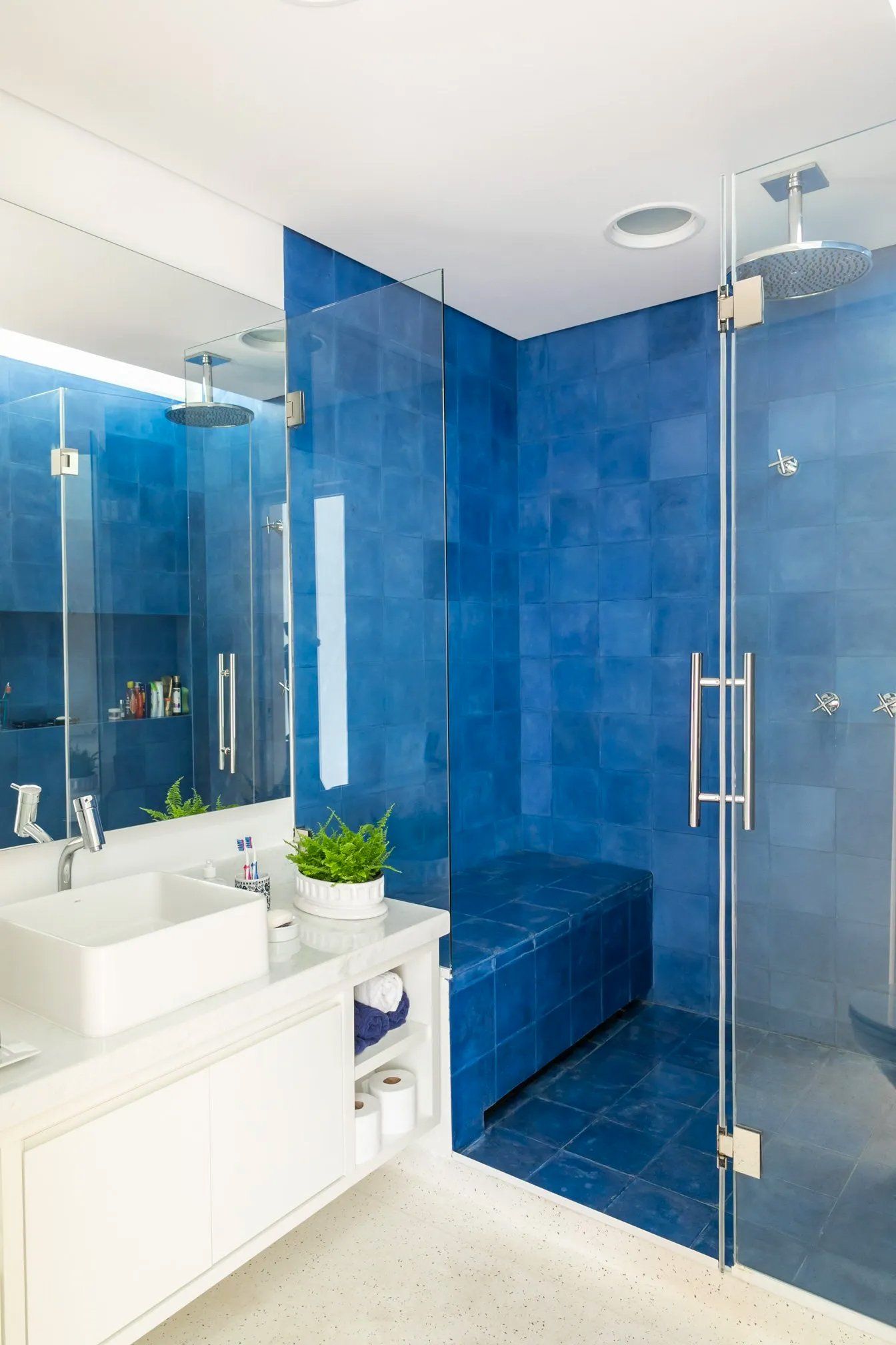 Um banheiro com azulejos azuis, pia, espelho e box amplo.