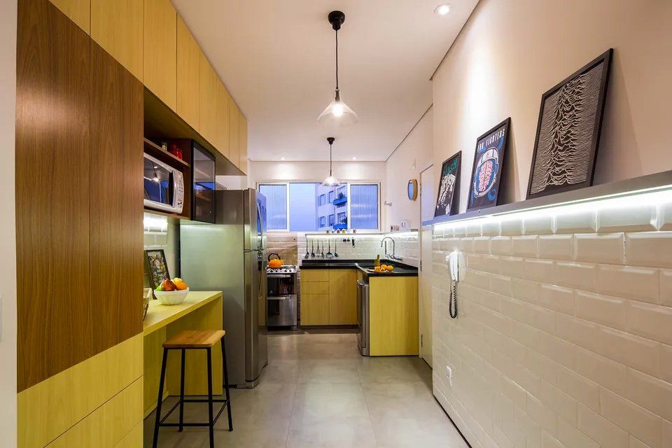 Uma cozinha com armários amarelos, eletrodomésticos de aço inoxidável, geladeira e micro-ondas.