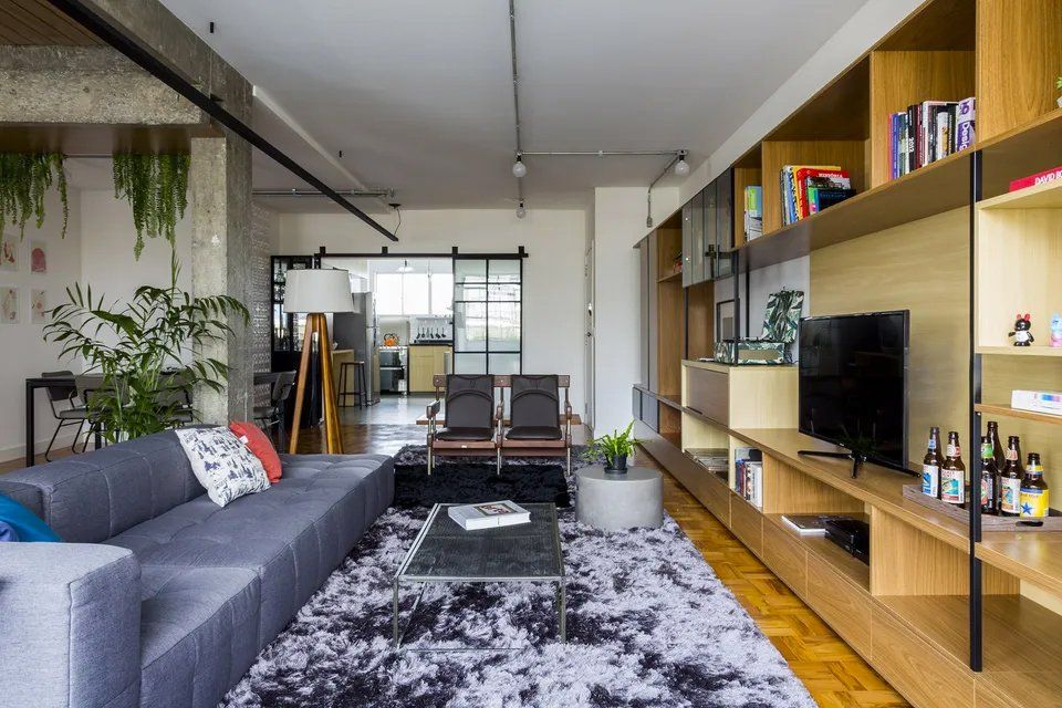 Uma sala com sofá, cadeiras, tapete e televisão.