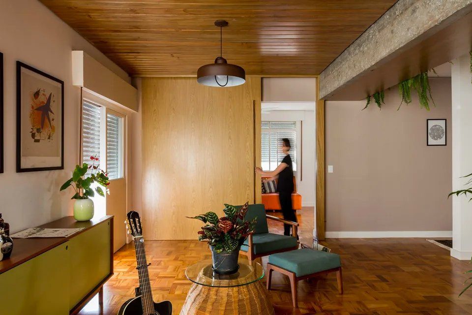 Uma sala de estar com um violão sobre uma mesa e uma mulher parada ao fundo.