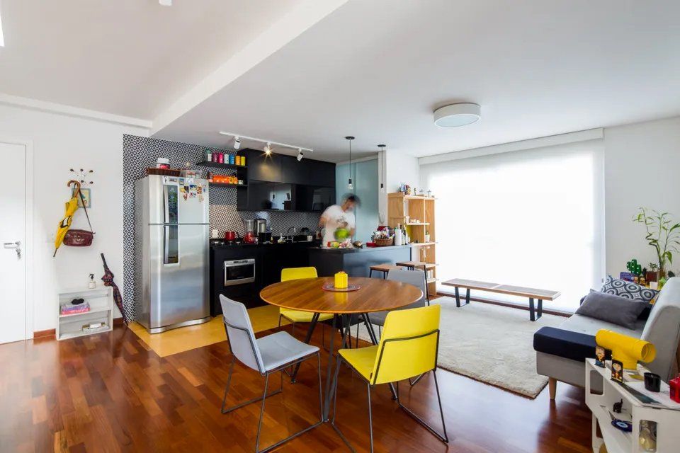 Uma sala com mesa e cadeiras e um homem na cozinha.