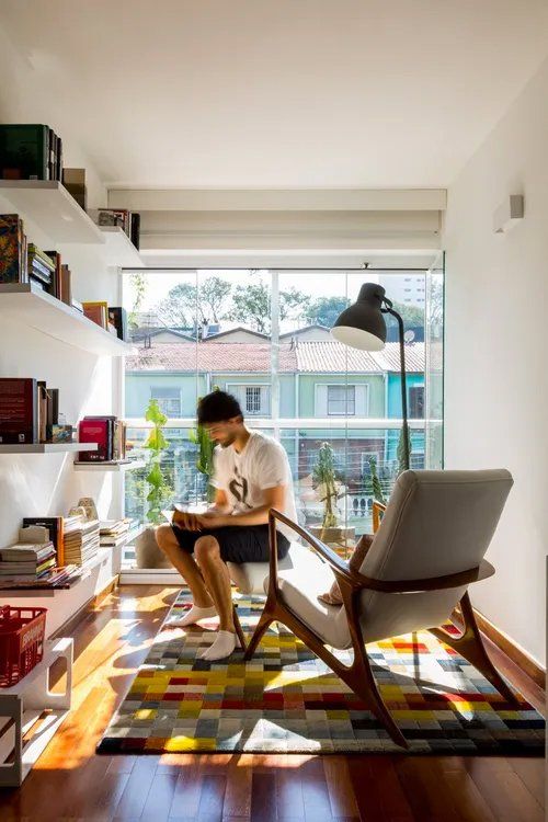 Um homem está sentado em uma cadeira lendo um livro em uma sala de estar.