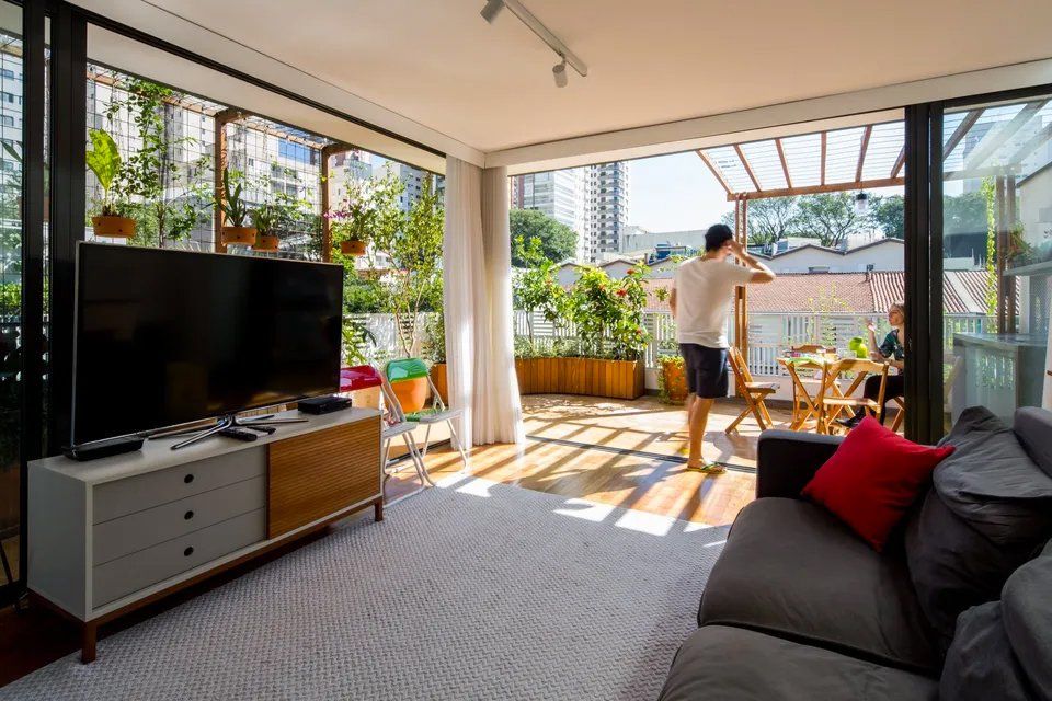 Um homem está na varanda de uma sala de estar com uma TV de tela plana.