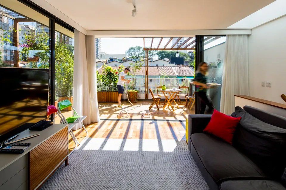 Uma sala de estar com sofá, televisão e portas de correr de vidro que dão acesso a uma varanda.