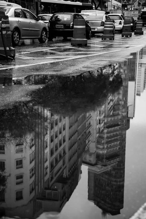 Uma foto em preto e branco de um estacionamento com carros e prédios refletidos na água