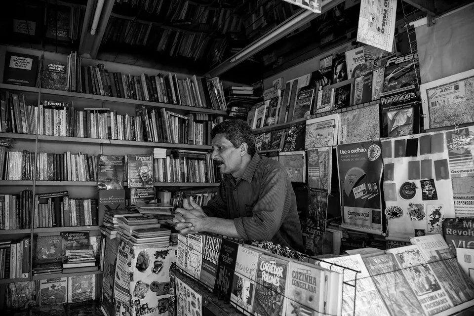 Um homem está sentado no balcão de uma livraria cercado de livros.