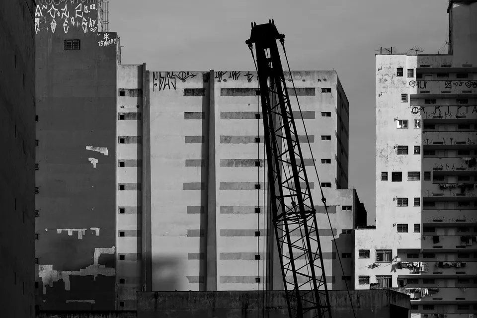 Uma foto em preto e branco de uma cidade com um guindaste em primeiro plano