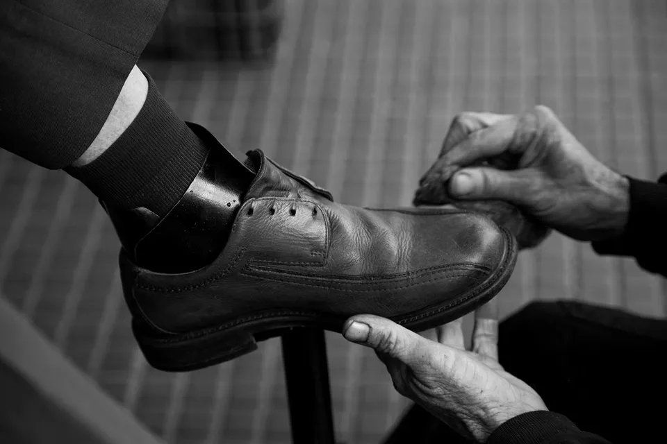 Uma pessoa está engraxando o sapato de outra pessoa em uma foto em preto e branco.