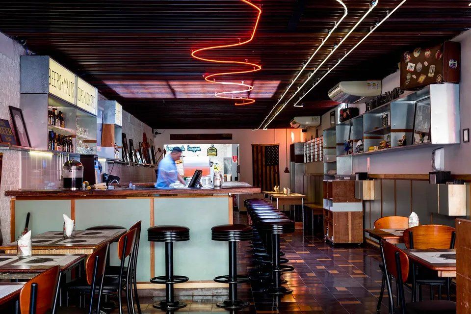 Um restaurante com mesas e cadeiras e um letreiro de néon no teto.