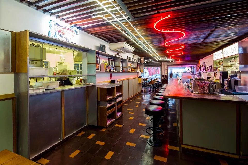 Um restaurante com um longo bar e um letreiro de neon acima dele.