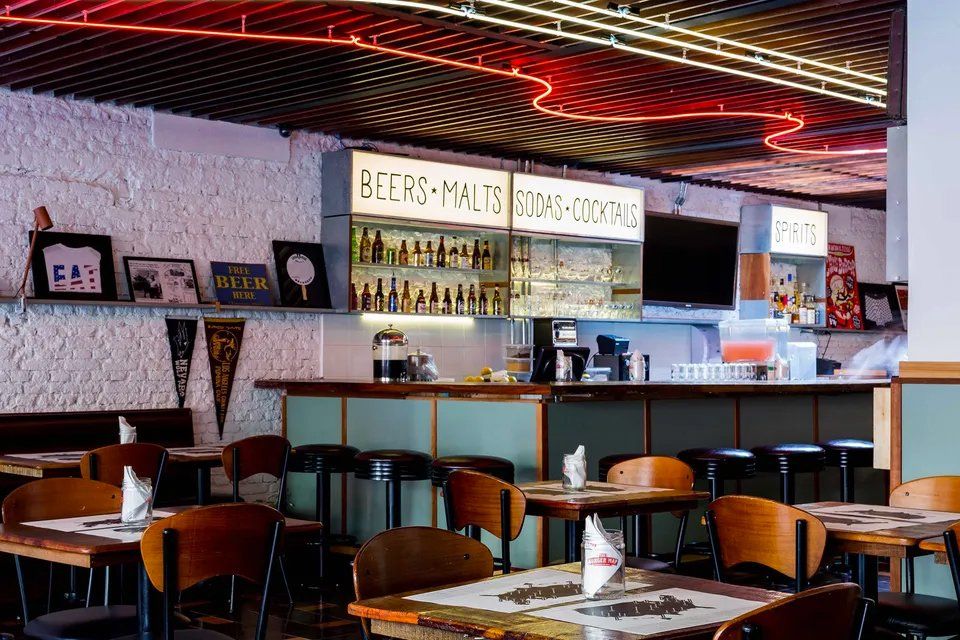 Um restaurante com mesas e cadeiras e um letreiro de néon no teto.