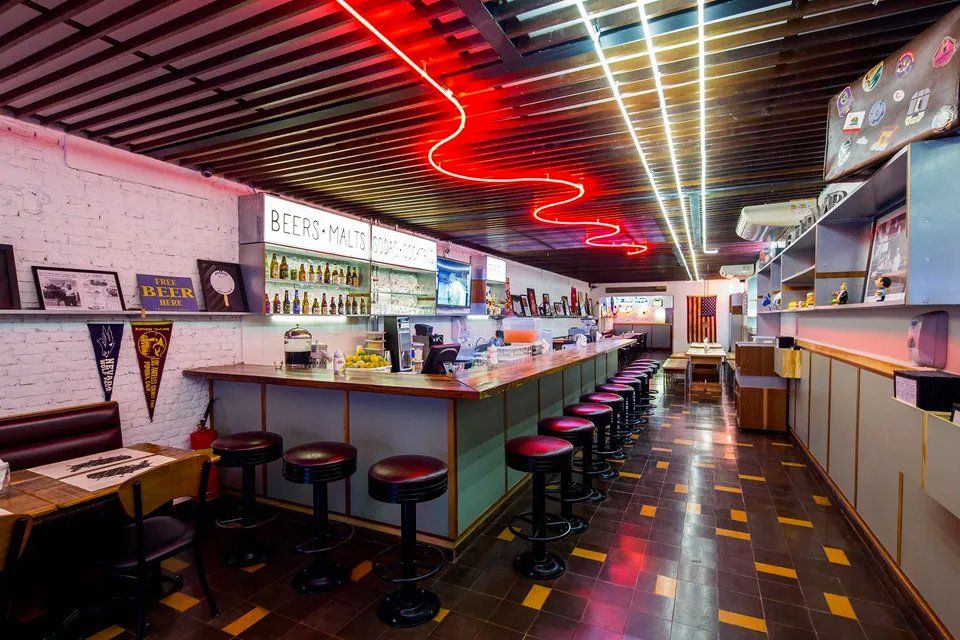 Um restaurante com um longo bar e bancos e um letreiro de néon no teto.