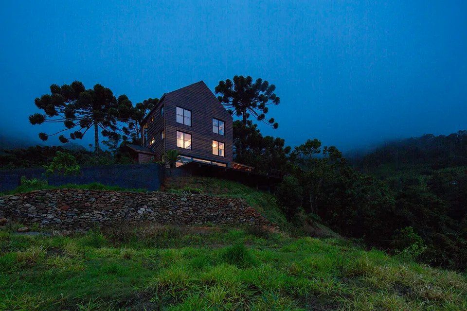 Uma casa está situada no topo de uma colina no meio de uma floresta à noite.