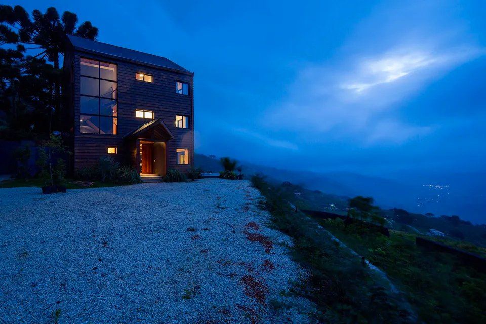 Uma grande casa é iluminada à noite no topo de uma colina.