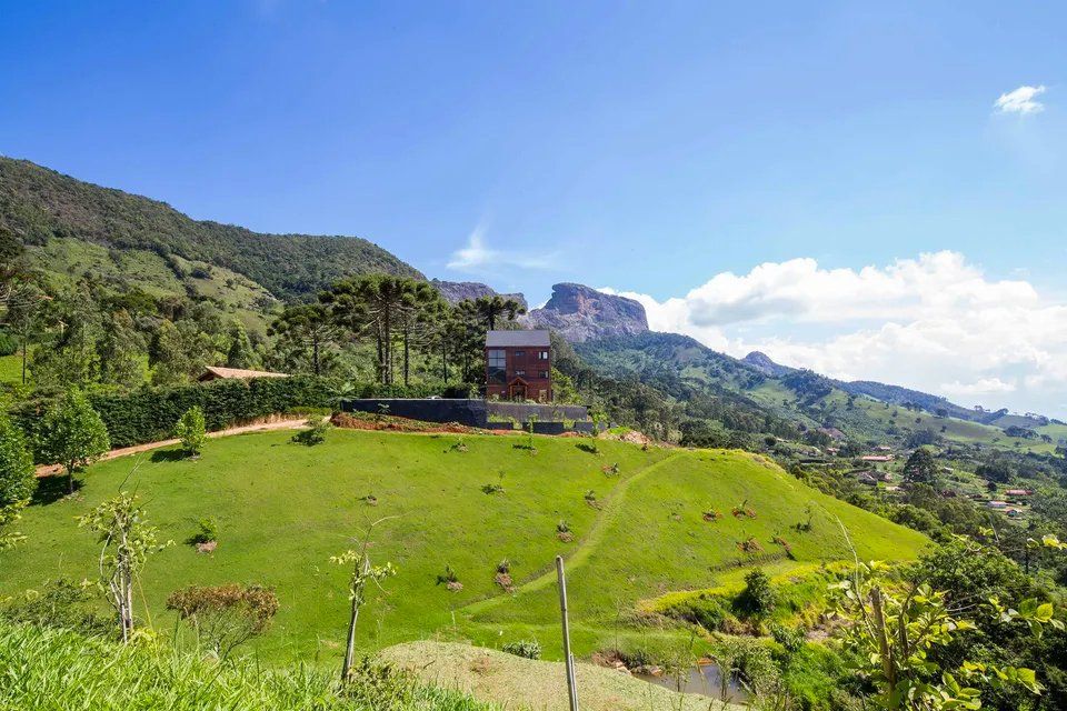 Uma casa está situada no topo de uma colina gramada cercada por montanhas.