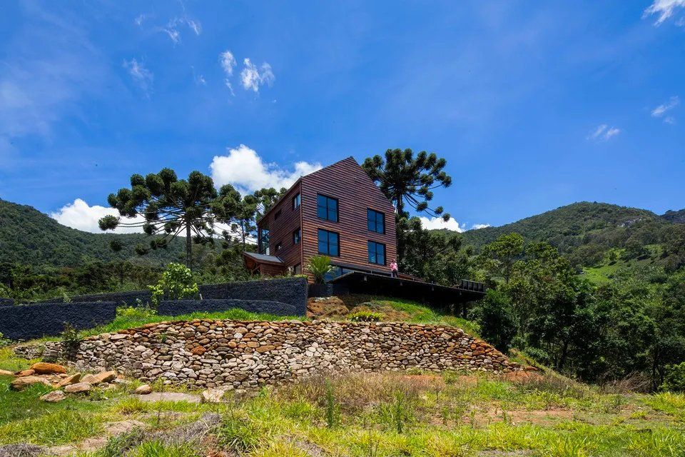 Uma casa está situada no topo de uma colina no meio de um campo cercado por árvores.