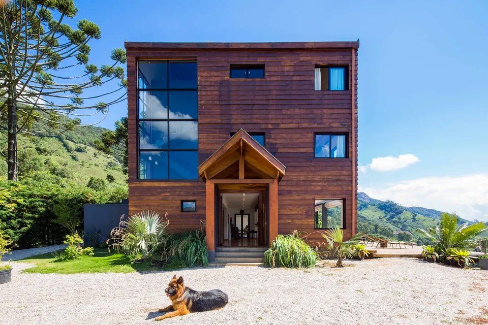 Um cachorro está deitado em frente a uma grande casa de madeira.