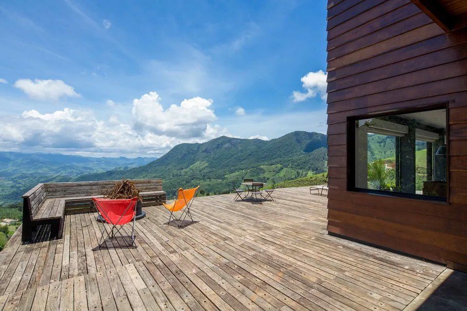 Um deck de madeira com cadeiras e um banco com vista para as montanhas.