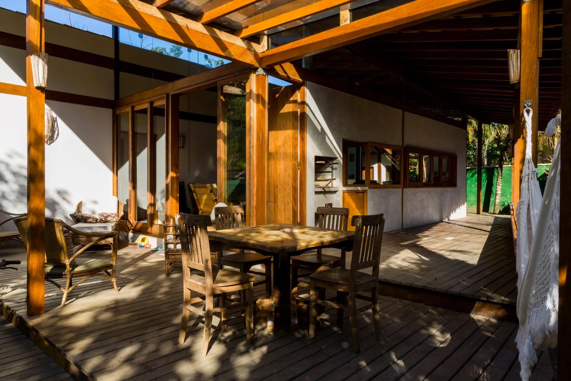 Um deck de madeira com mesa e cadeiras sob uma pérgula.