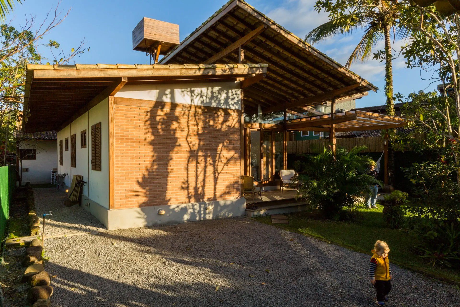 Uma menina está parada em frente a uma casa de tijolos com telhado de madeira.