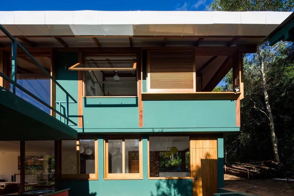 Uma casa verde com telhado branco é cercada por árvores.