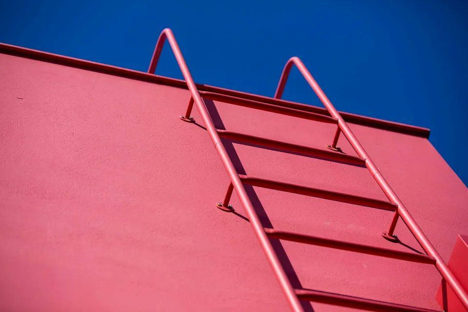 Uma escada vermelha está presa à lateral de um prédio vermelho