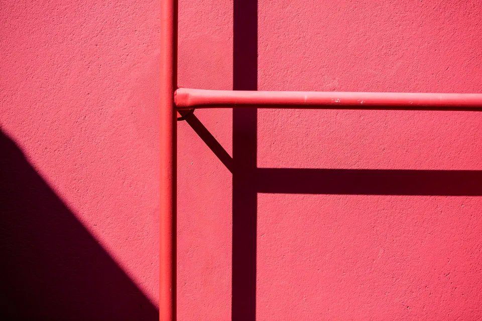 Um close de uma parede vermelha com a sombra de uma grade.