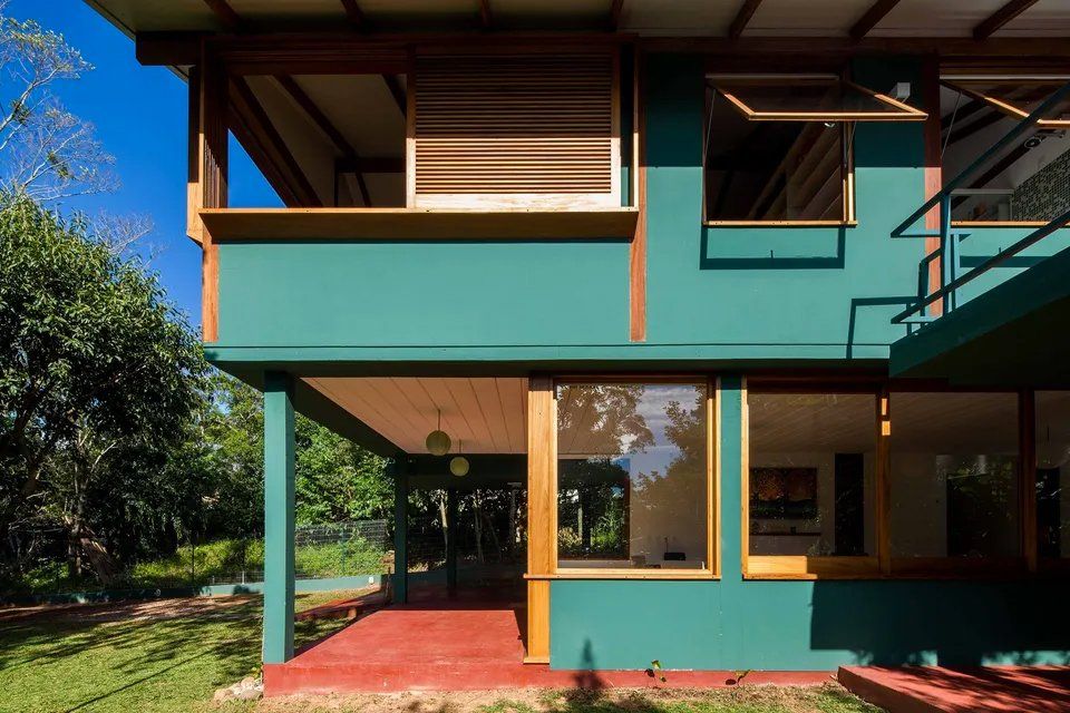 Uma casa verde com muitas janelas e árvores ao fundo