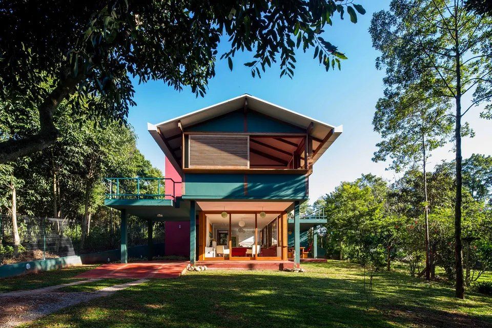 Uma casa azul e vermelha está cercada por árvores e grama.