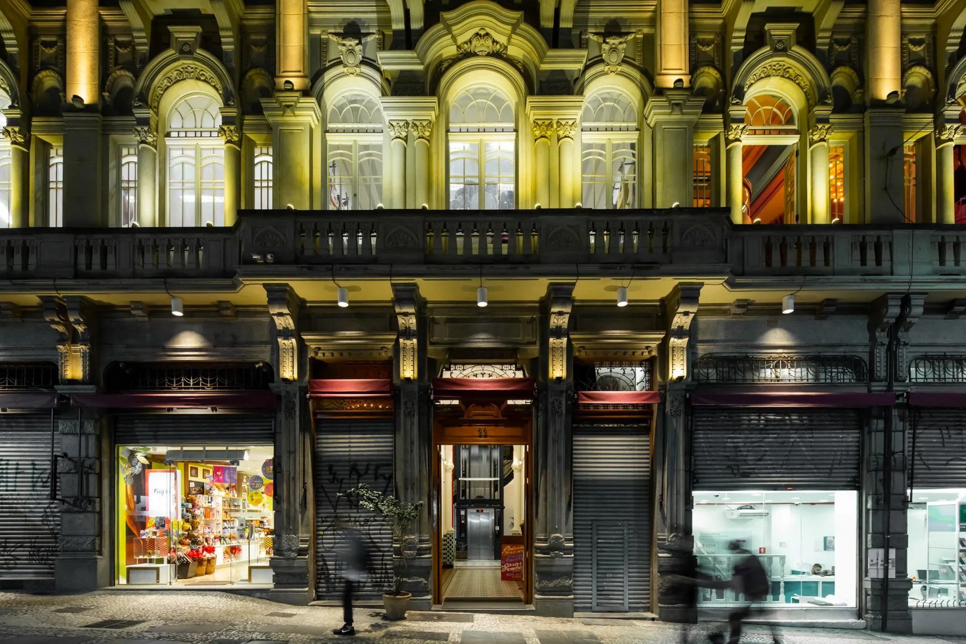 Um grande prédio com varanda e pessoas andando em frente à noite.