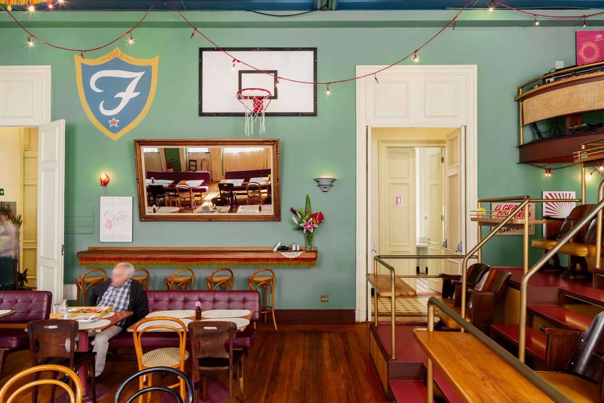 Um homem está sentado à mesa de um restaurante com uma cesta de basquete na parede.