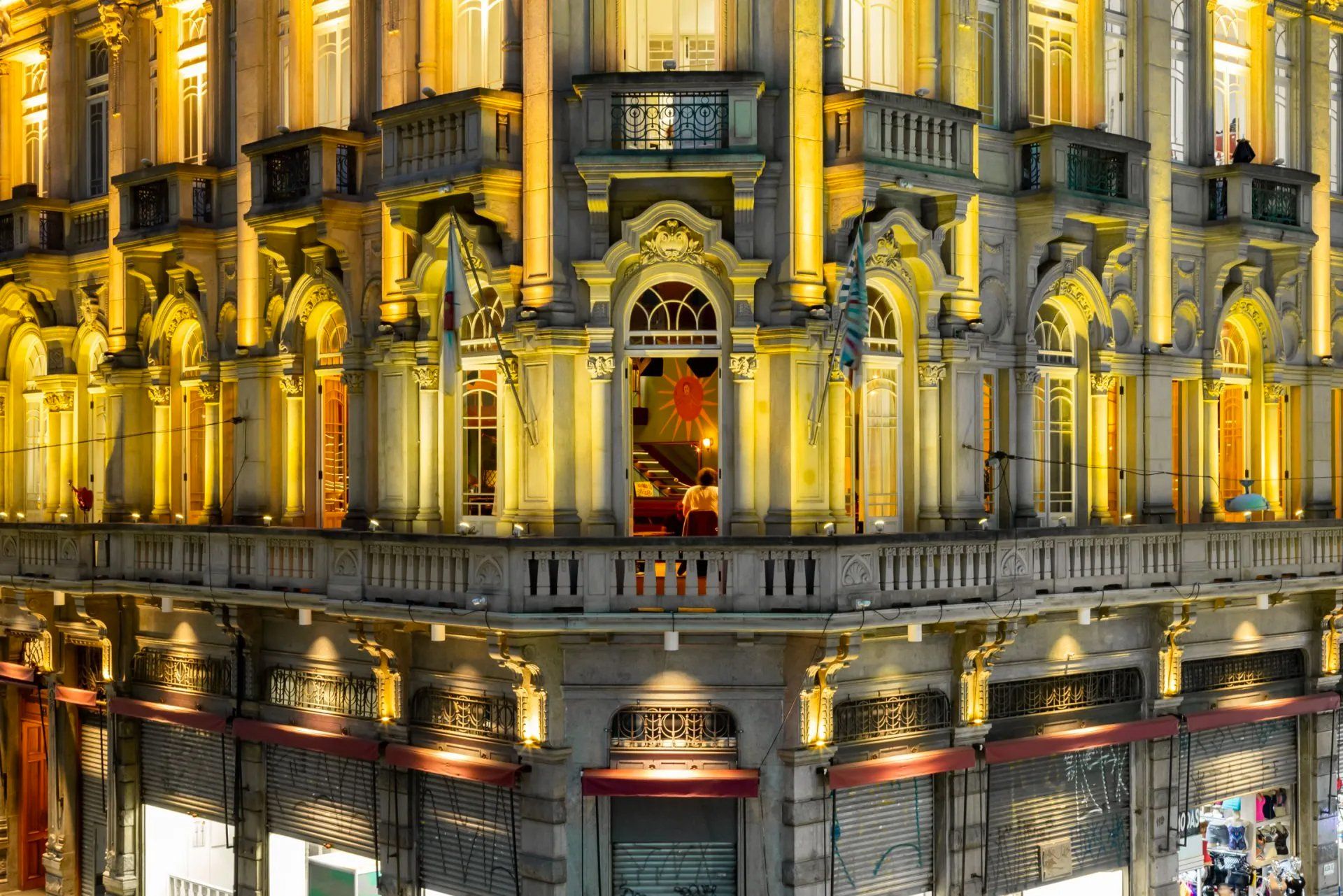 Um grande edifício com varanda e muitas janelas fica iluminado à noite.