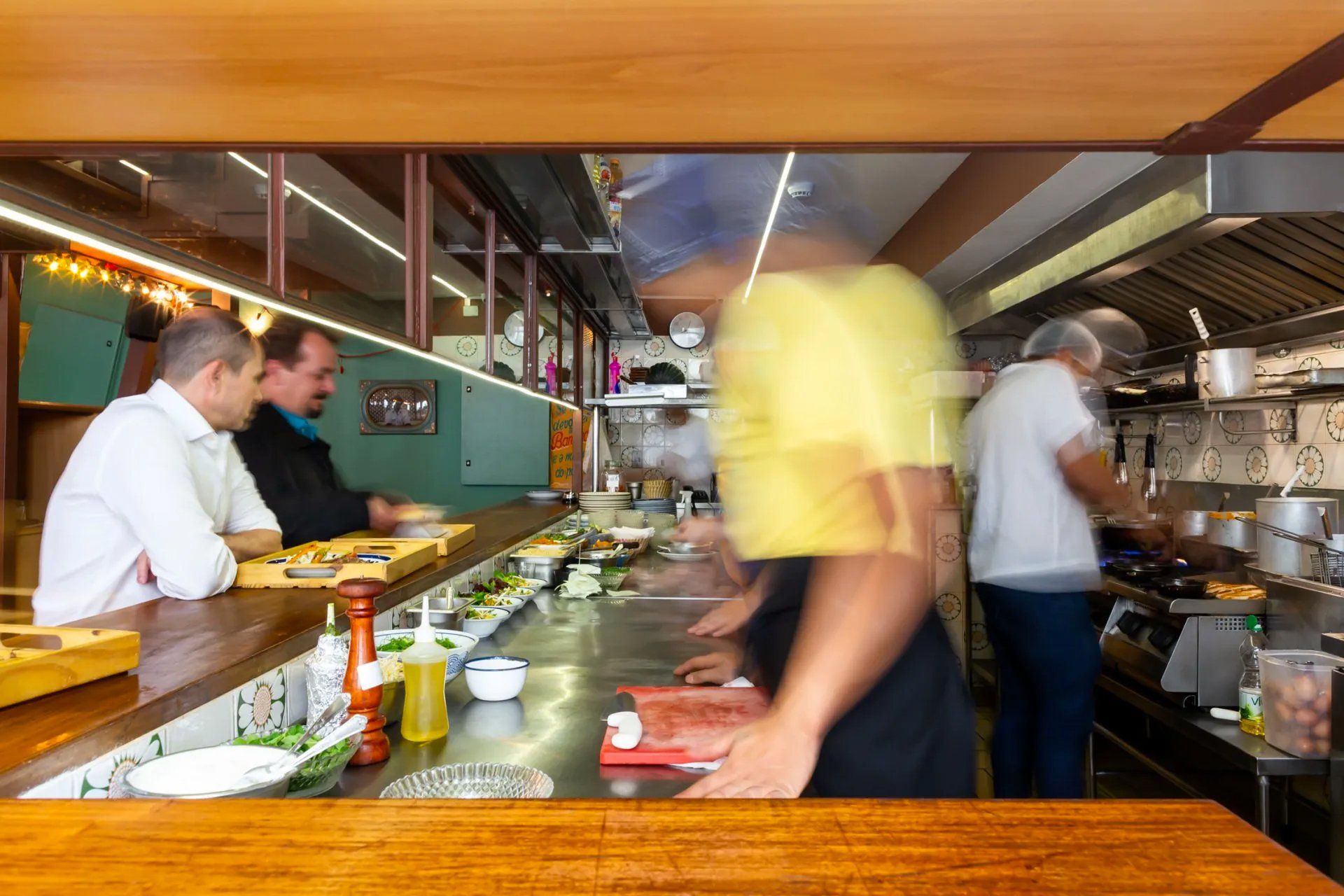 Um grupo de pessoas está sentado à mesa na cozinha de um restaurante.