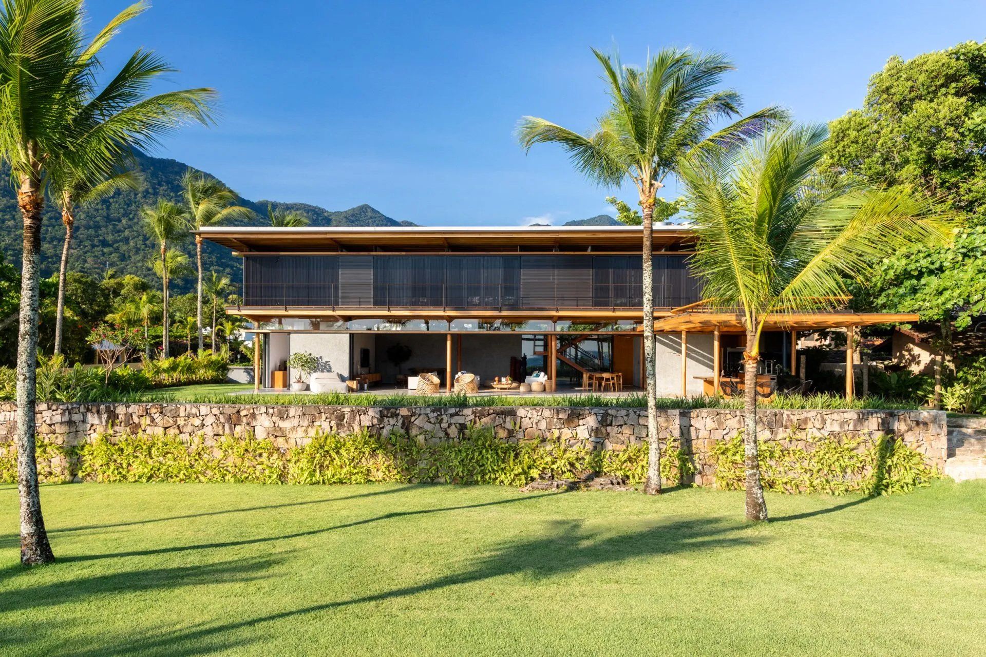 Uma grande casa é cercada por palmeiras e montanhas.