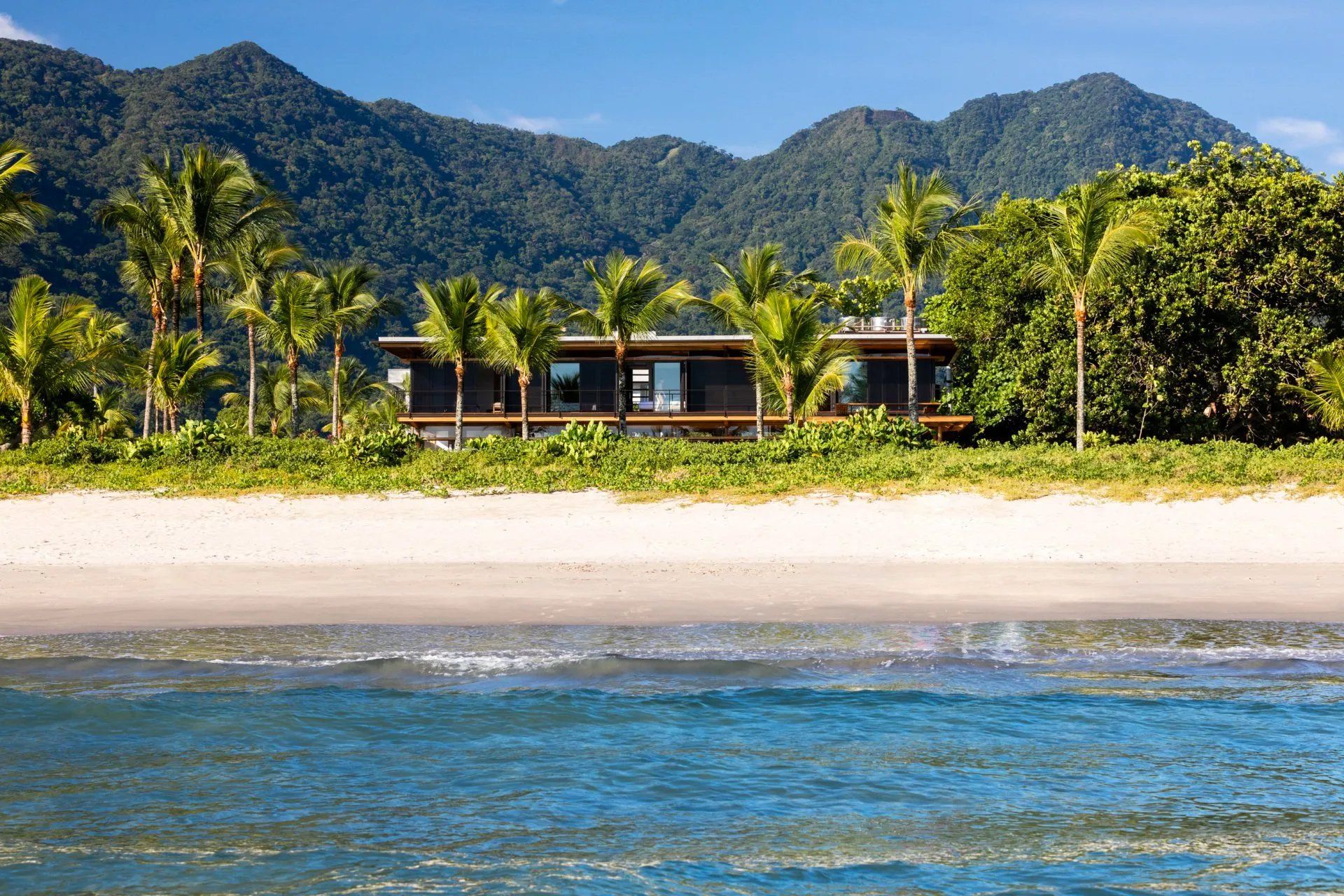 Uma praia com uma casa ao fundo e montanhas ao fundo