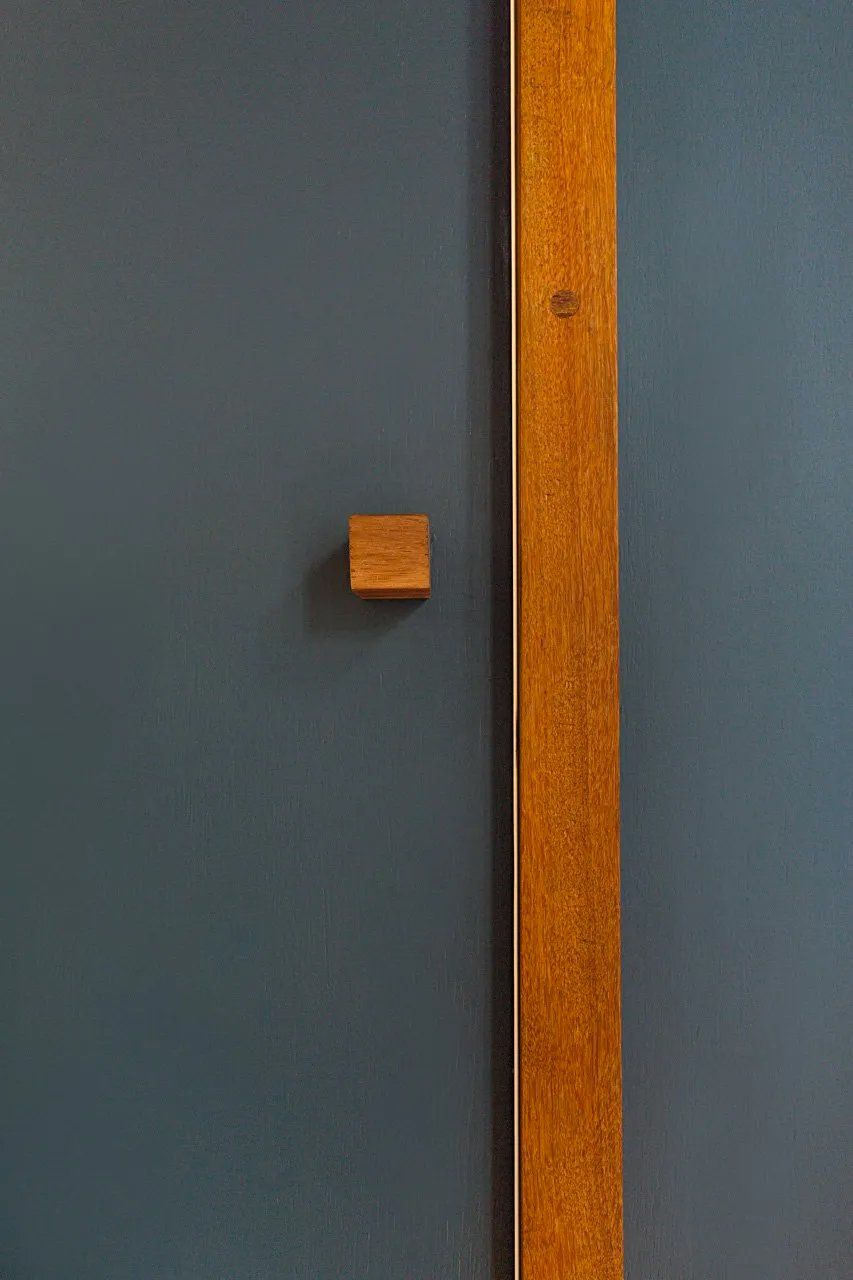Uma porta de madeira com maçaneta de madeira está encostada em uma parede azul.