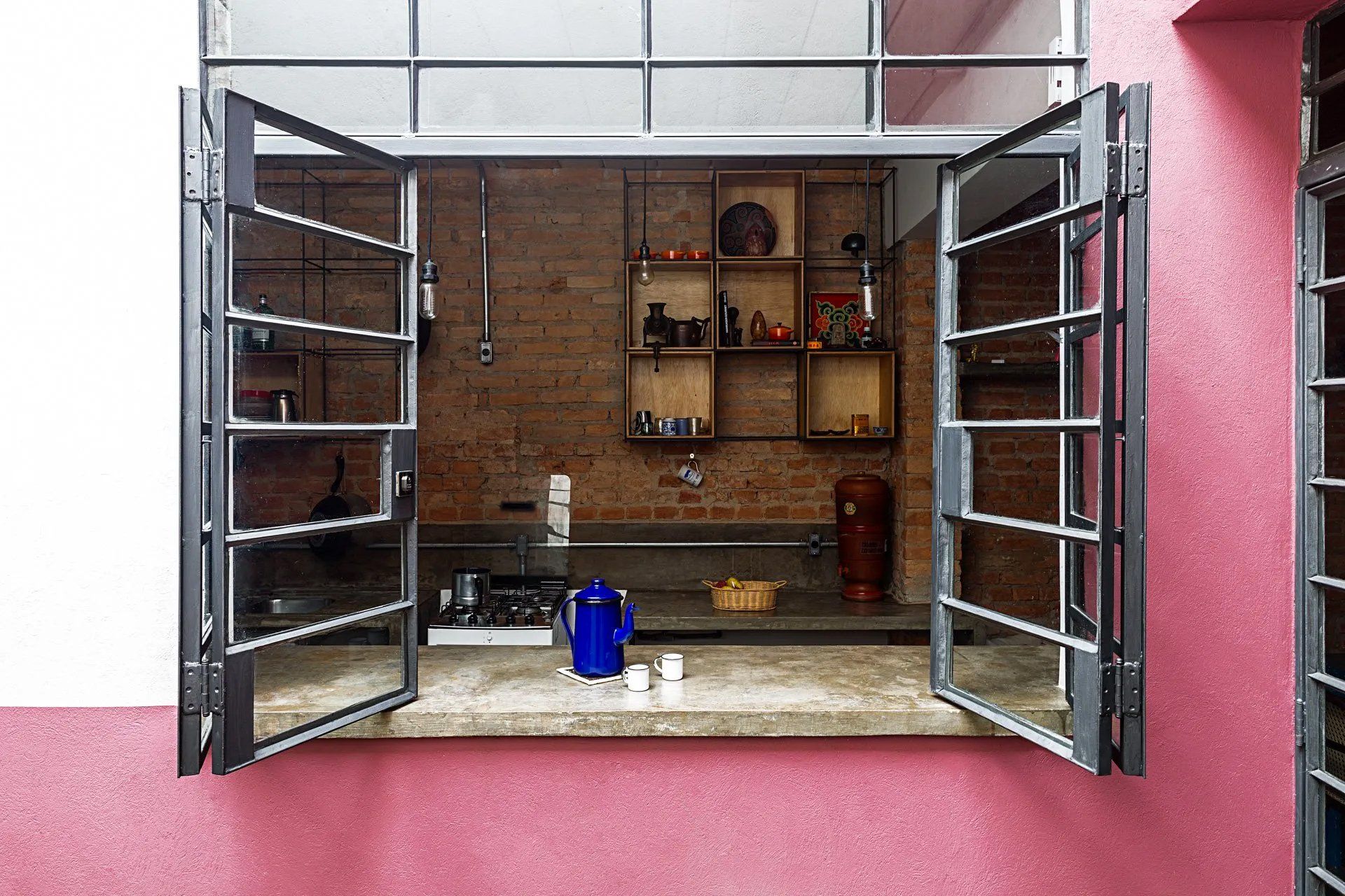 Uma cozinha com janela aberta e uma panela azul na bancada.