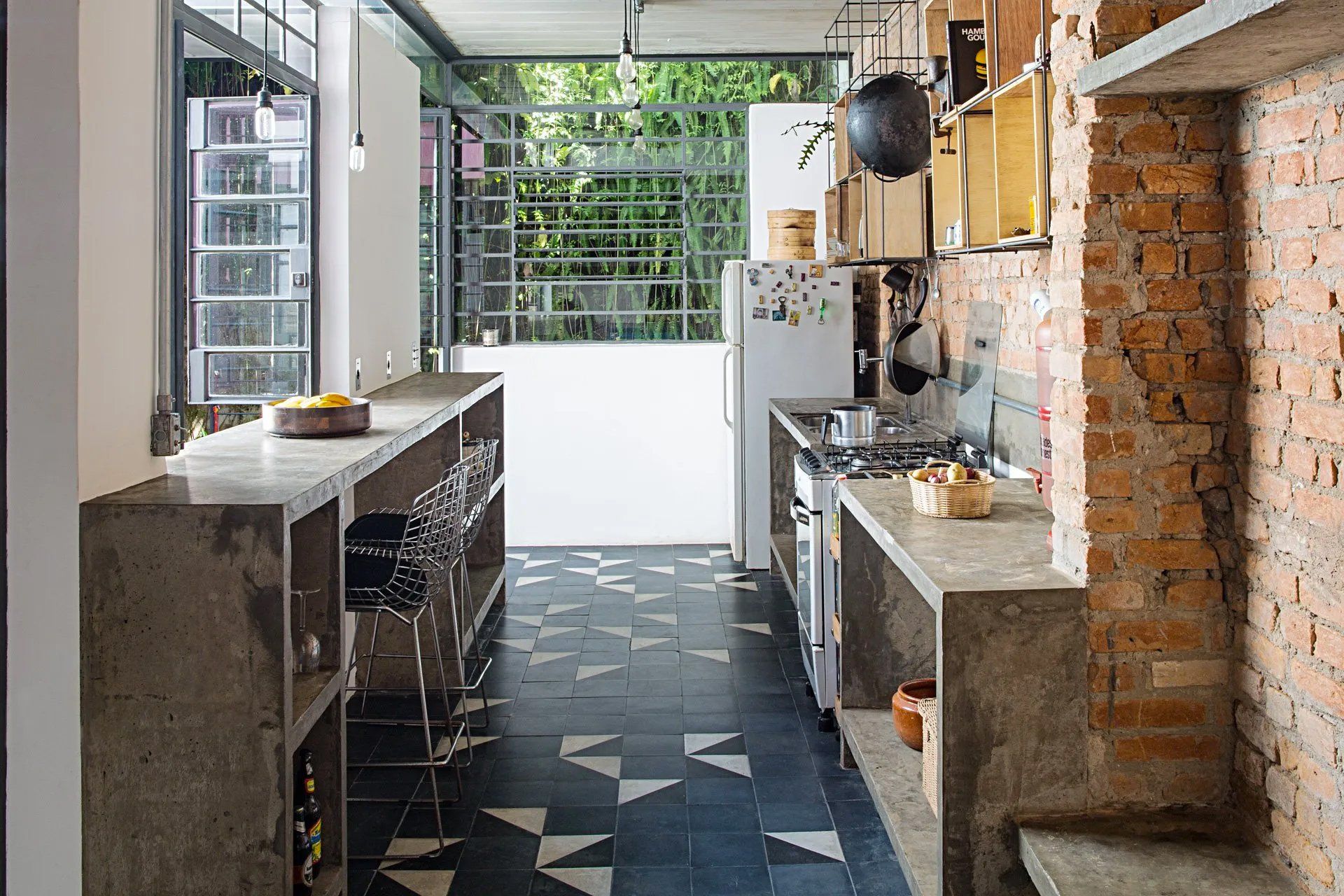 Uma longa cozinha com parede de tijolos e piso de cerâmica preta e branca.