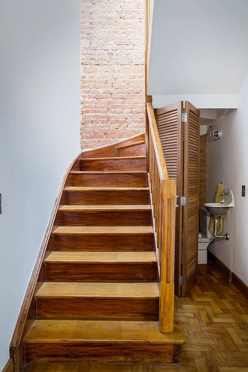 Uma escada de madeira que leva a um banheiro com parede de tijolos.