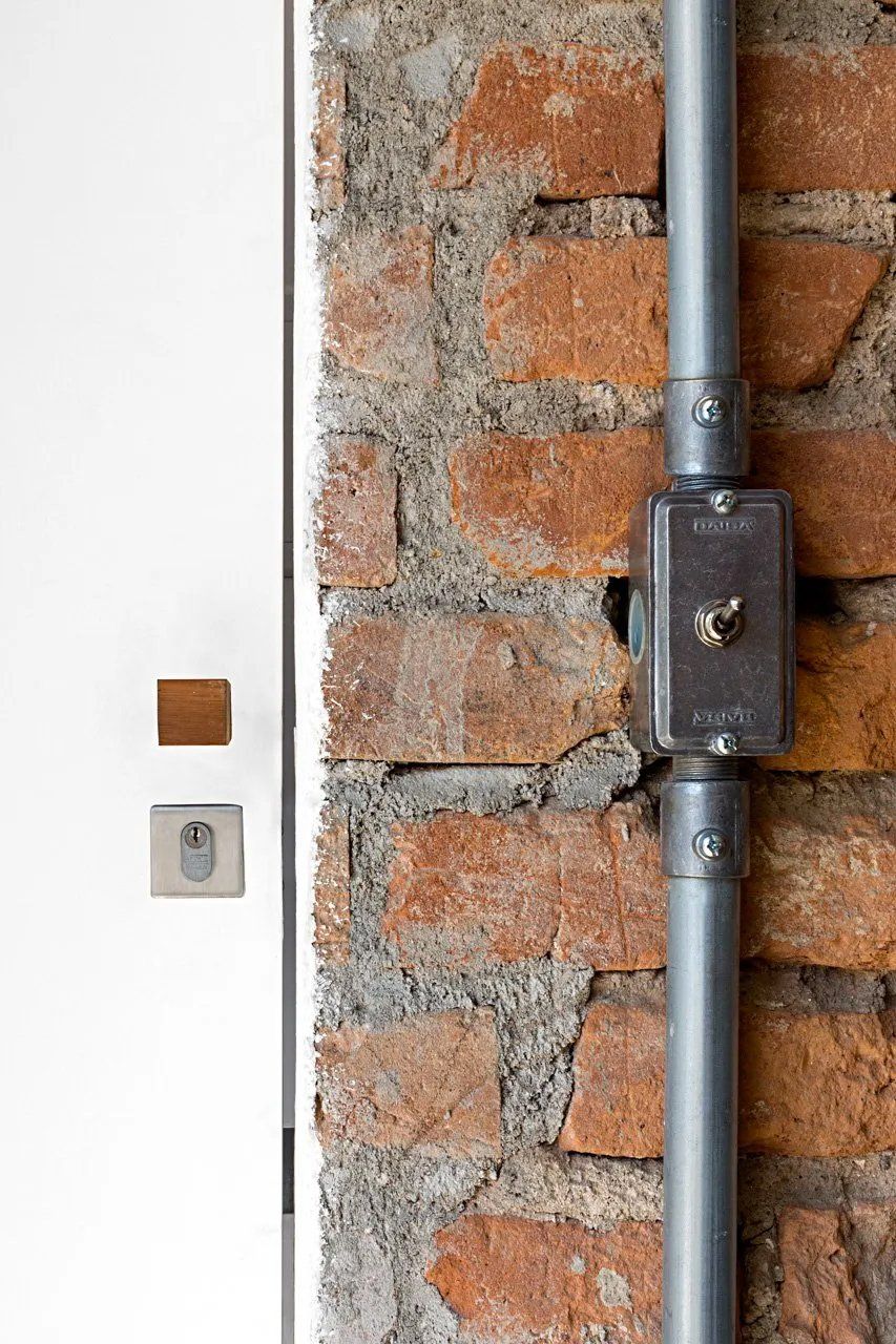 Uma parede de tijolos com um tubo de metal e um interruptor.